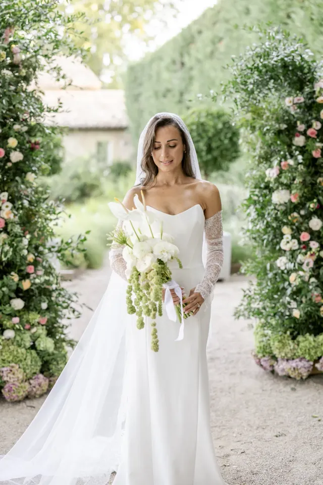 La mariée et son bouquet dans l'allée de rosiers du mas