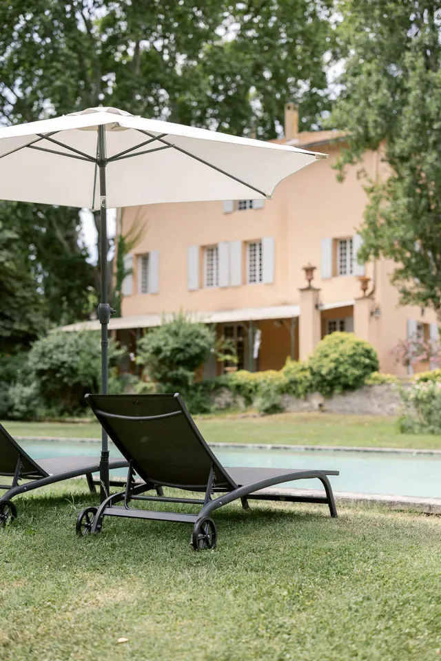 Transats au bord de la piscine face à la bastide
