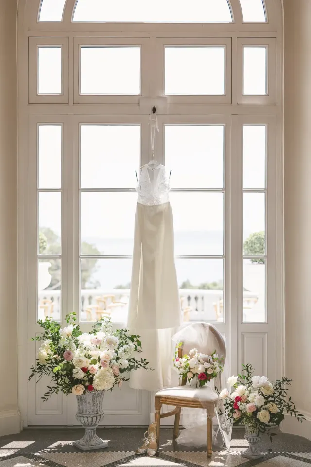 Robe de mariée suspendue devant une fenêtre ouverte sur la baie