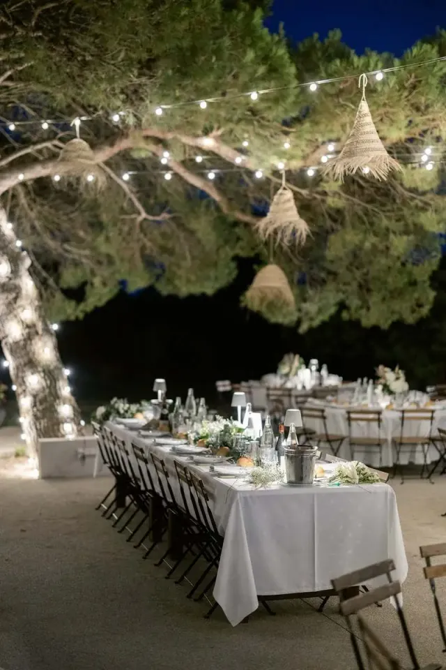 Longue table de mariage dressée sous un pin, guirlandes lumineuses à la tombée de la nuit en Provence